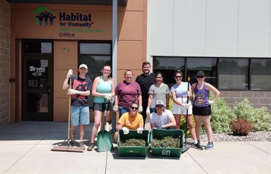 A group of people in front of a Habitat for Humanity office behind two bins full of grass and soil