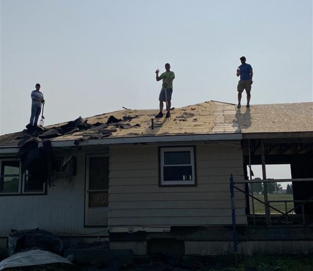 3 people on a roof cleaning off debris